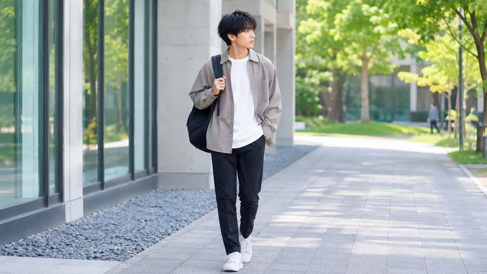 大学構内を歩く日本人大学生の、白Tシャツとグレーの羽織り、黒パンツを合わせたメンズマネキン買いコーデ